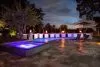 Luxurious outdoor pool with glowing spa, fire features, and elegant nighttime ambiance.