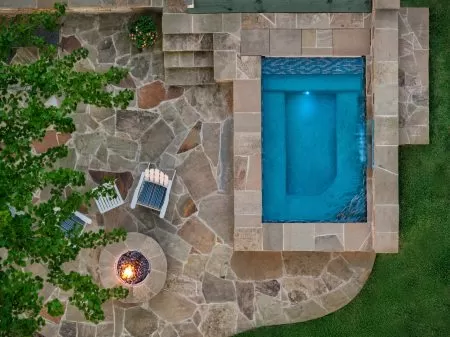 Small spa pool with stone waterfall and fire pit overlooking lake in wooded backyard